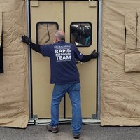 Un homme termine d'installer une tente médicale beige