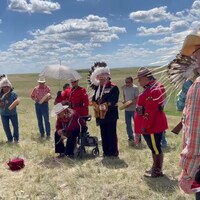 Des membres de la Nation Blood en habits traditionnels se recueillent devant une boîte dans un paysage de prairie.