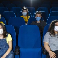 Quelques spectateurs portant des masques assis dans une salle de spectacle pratiquement vide.
