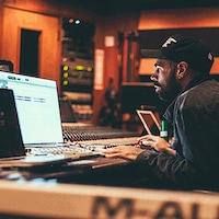 Un homme portant une casquette assis devant un ordinateur dans un studio d'enregistrement.