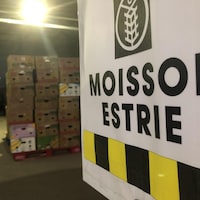 Une affiche de Moisson Estrie devant un local plein de boîtes.