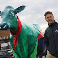 Michel-Olivier Matte aux côtés d'une sculpture de vache décorée et peinturée.