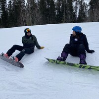 Deux femmes assises sur la neige avec leurs planches à neige. 
