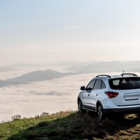 Un véhicule utilitaire sport sur le bord d'un ravin avec un paysage de montagnes et de nuages en arrière-plan.