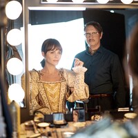 Une femme, dans une robe de reine, assise devant un miroir de maquillage.