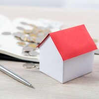 Une petite maison en carton, une calculatrice, un livre de comptes, un stylo et des pièces de monnaie sont déposés sur une table afin de représenter la hausse des taux d’intérêt sur les emprunts hypothécaires.