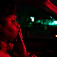 Une femme, dans sa voiture, de profil, sous un éclairage rouge.