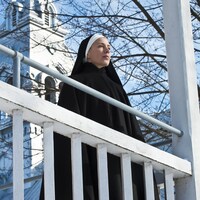 Une religieuse regarde au loin, sur un balcon.