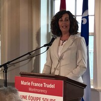 Marie France Trudel devant les drapeaux québécois et canadiens, lors d'un discours.