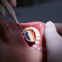 Gros plan sur le visage d'une femme qui ouvre la bouche pendant que des mains gantées font un examen dentaire avec un miroir