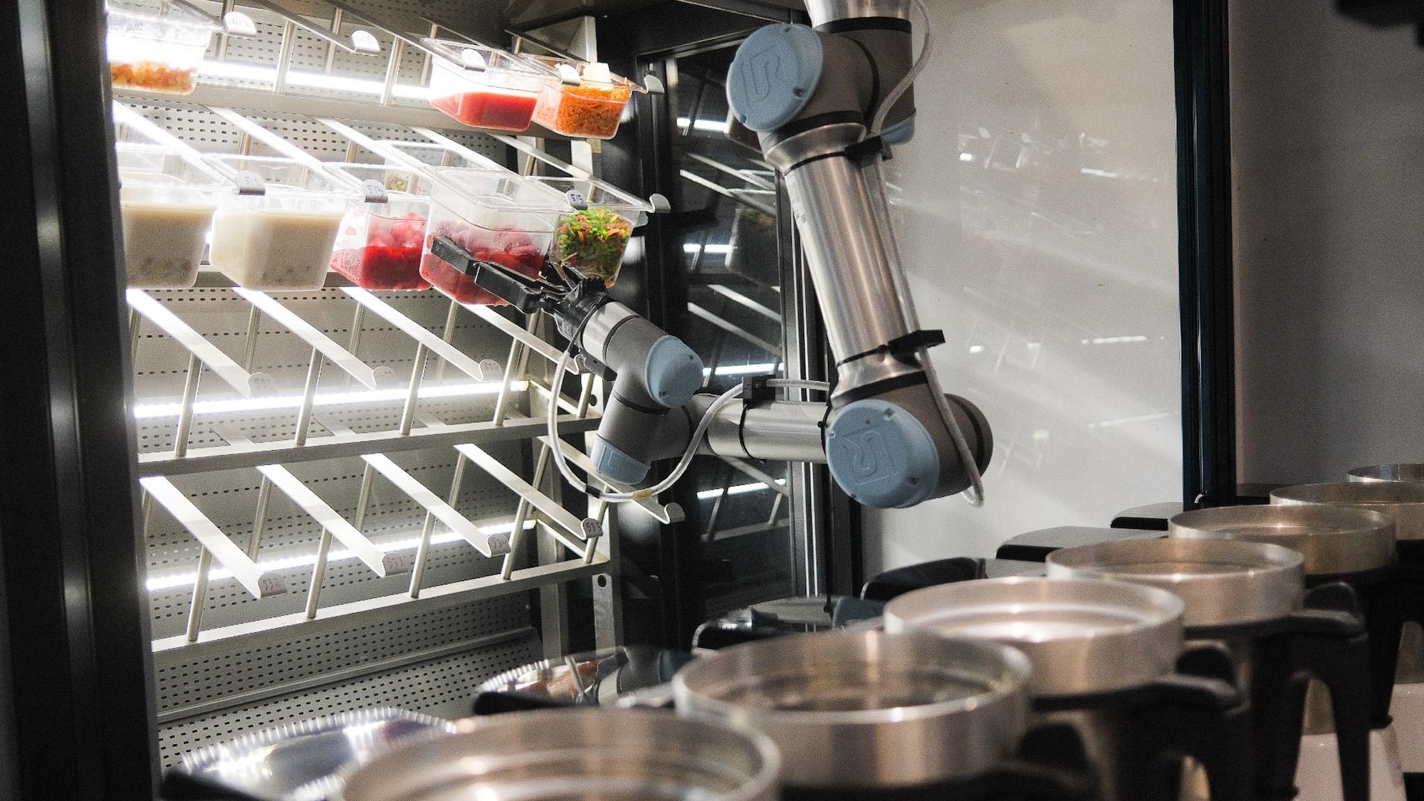 Un robot prend des bacs plein d'aliments dans une cuisine.