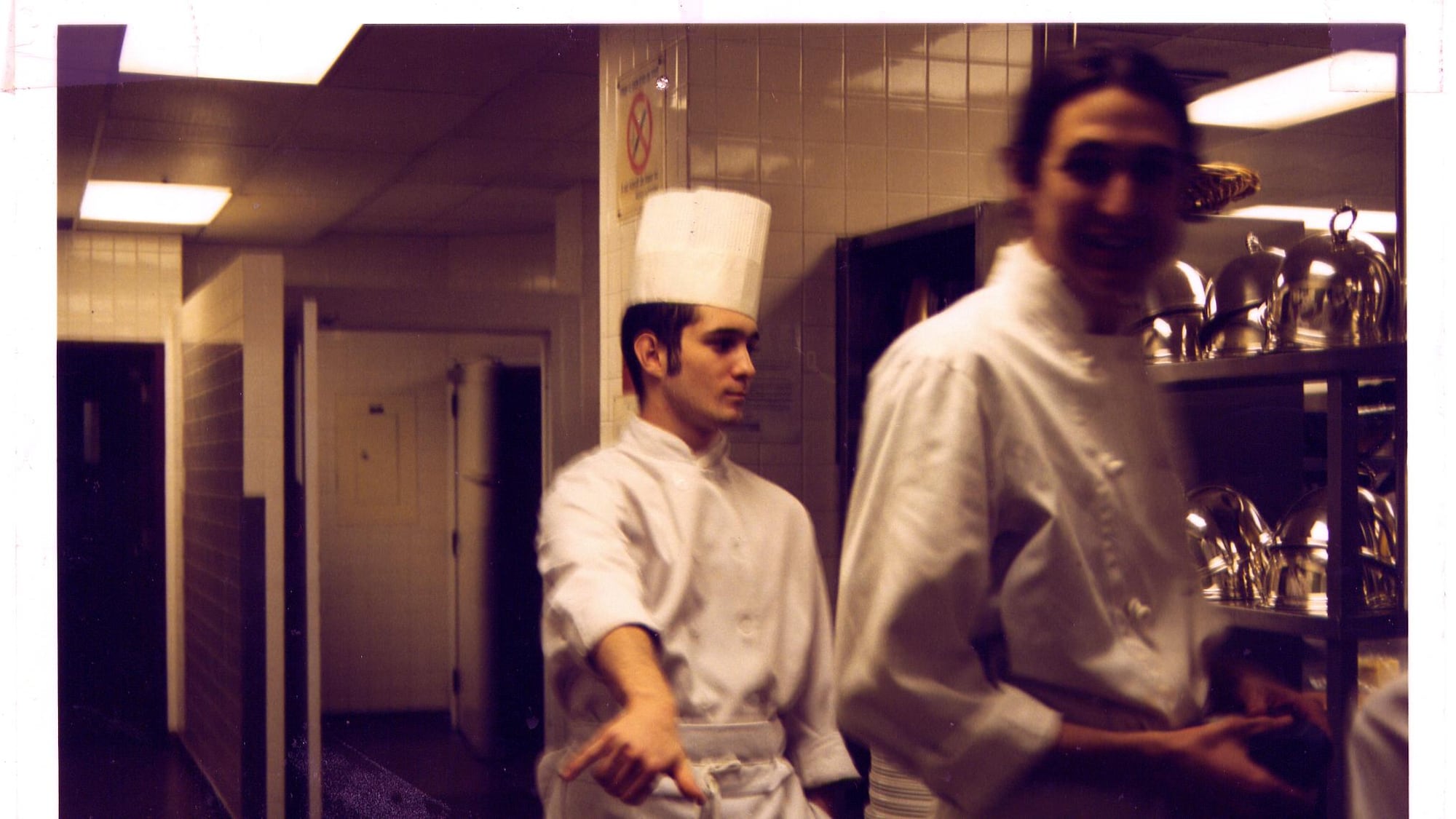 Bob est flou et regarde la caméra en souriant. Derrière lui, un autre apprenti-chef portant une toque de dirige vers la cuisine.