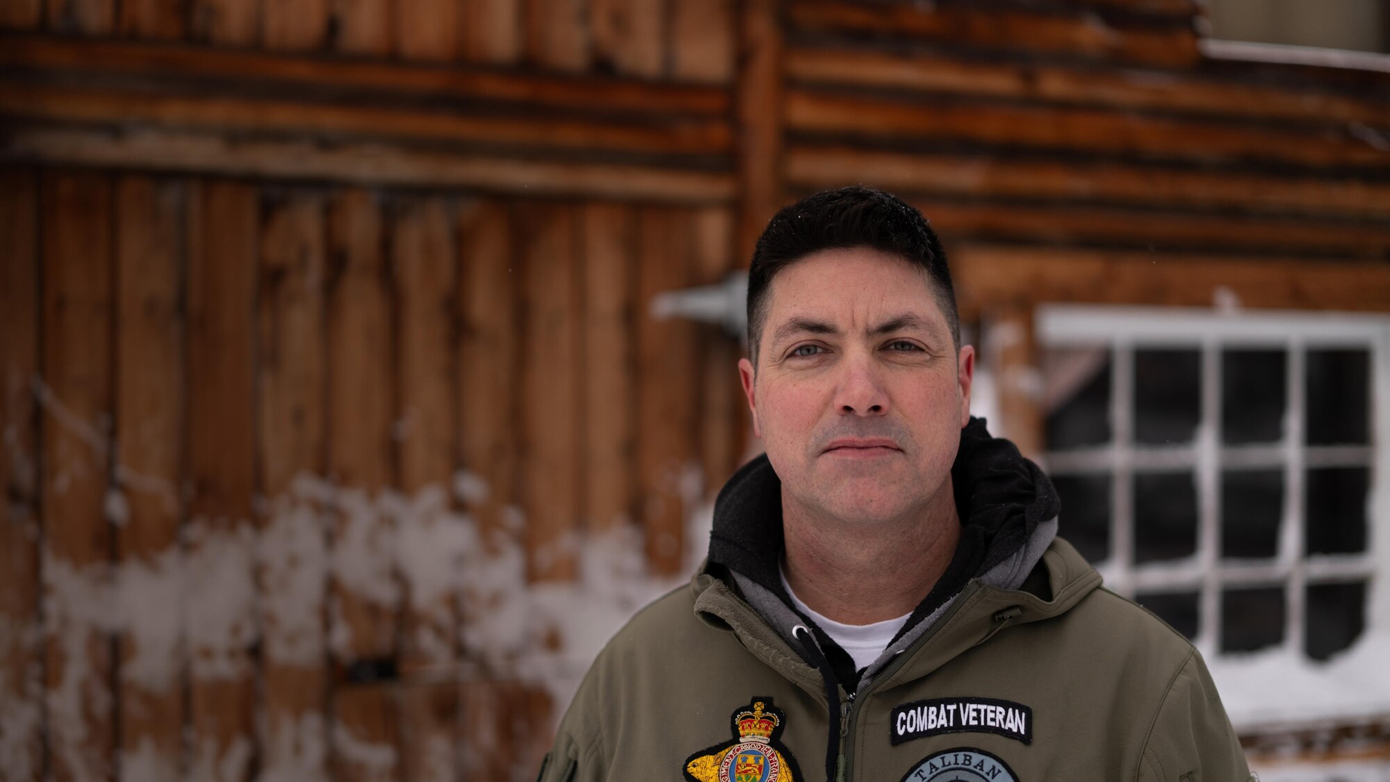 Portrait de Patrick Lemay à l'extérieur de sa cabane au Yukon. Il porte un manteau rempli d'écussons.