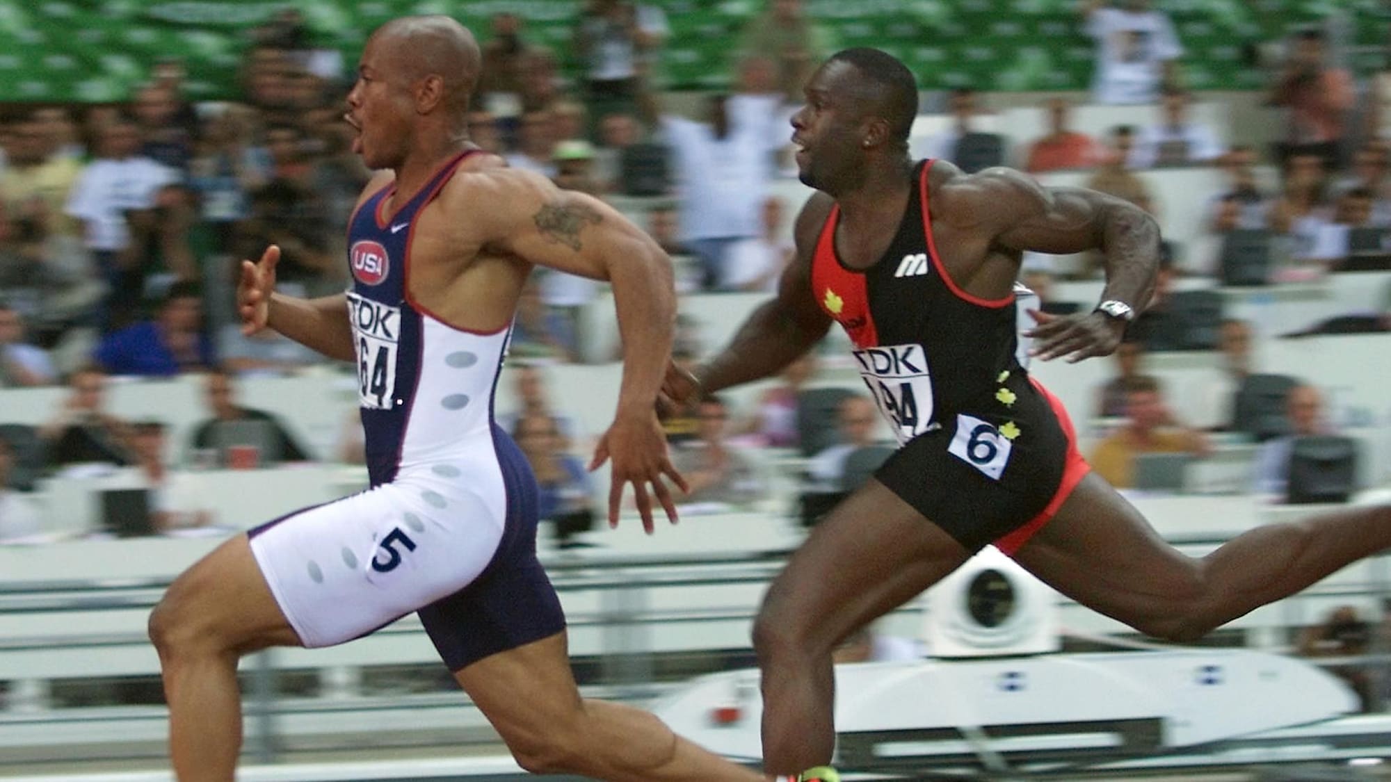 Un sprinteur en bleu en devance un autre en tenue rouge et noire. 