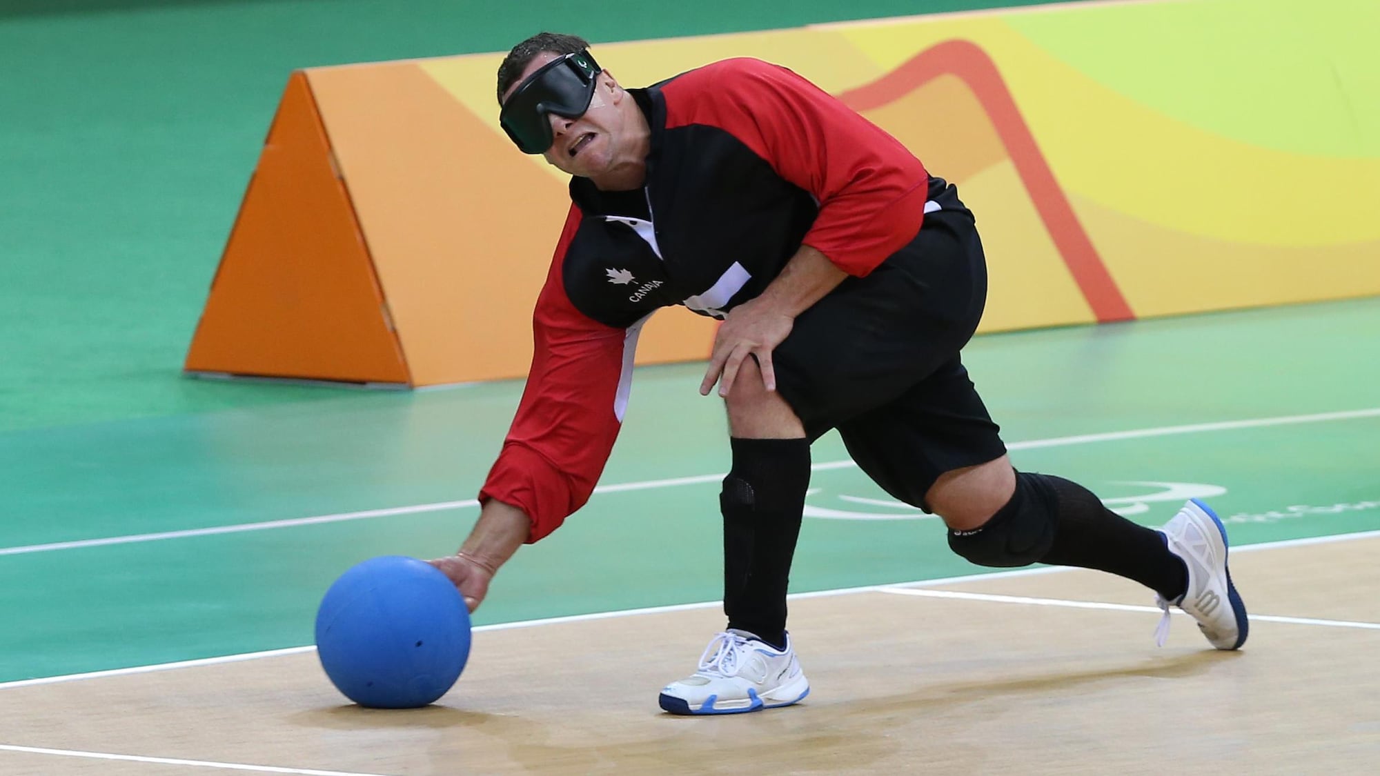 Il lance un ballon à la manière d'une boule de quilles pendant un match de goalball