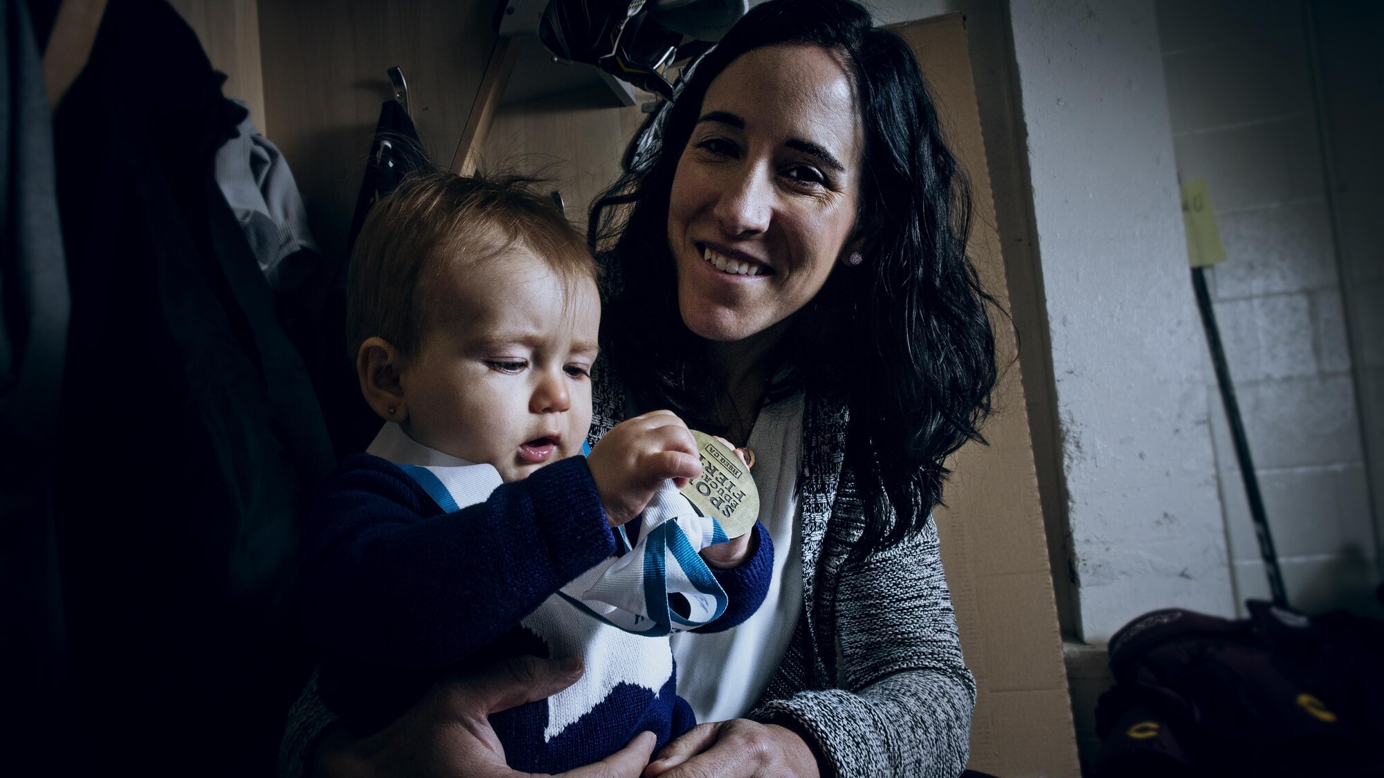 Caroline Ouellette tient sa fille Liv qui, elle, tient et regarde une médaille.