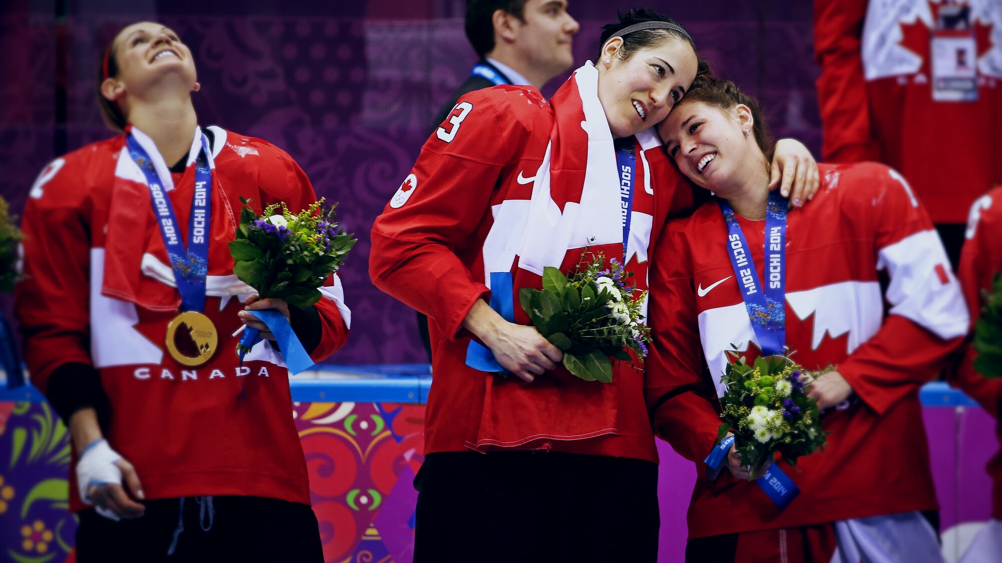 Meaghan Mikkelson, Caroline Oullette et Melodie Daoust, médaille d'or au cou et bouquet de fleurs à la main, se tiennent debout sur la glace après avoir remporté la finale olympique.