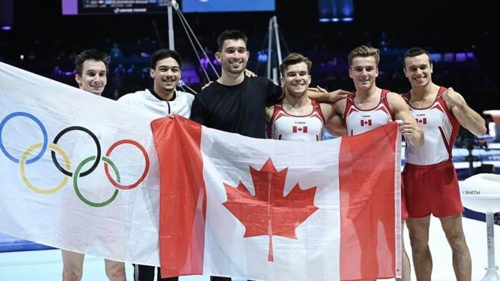 Des gymnastes prennent la pose avec un drapeau canadien et un autre des Jeux olympiques. 