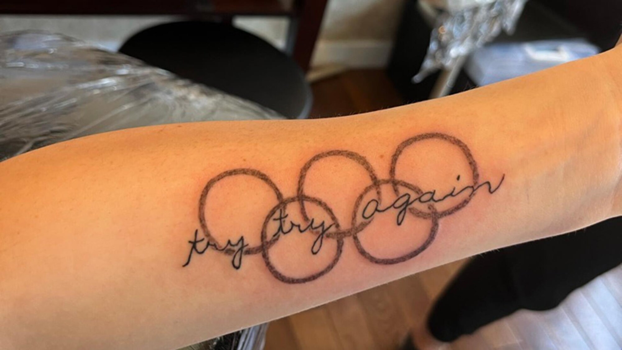 Un tatouage sur un bras avec les cinq anneaux olympiques et les mots : try rty again