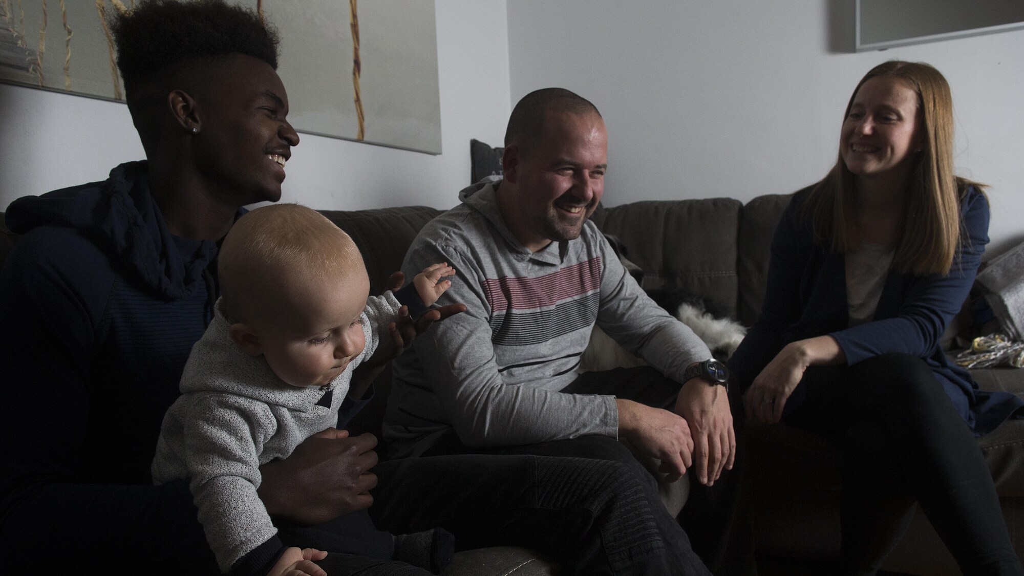 Prinzy Dessources, qui tient dans ses bras le petit Madden, est assis sur un divan près de son père et de sa mère.