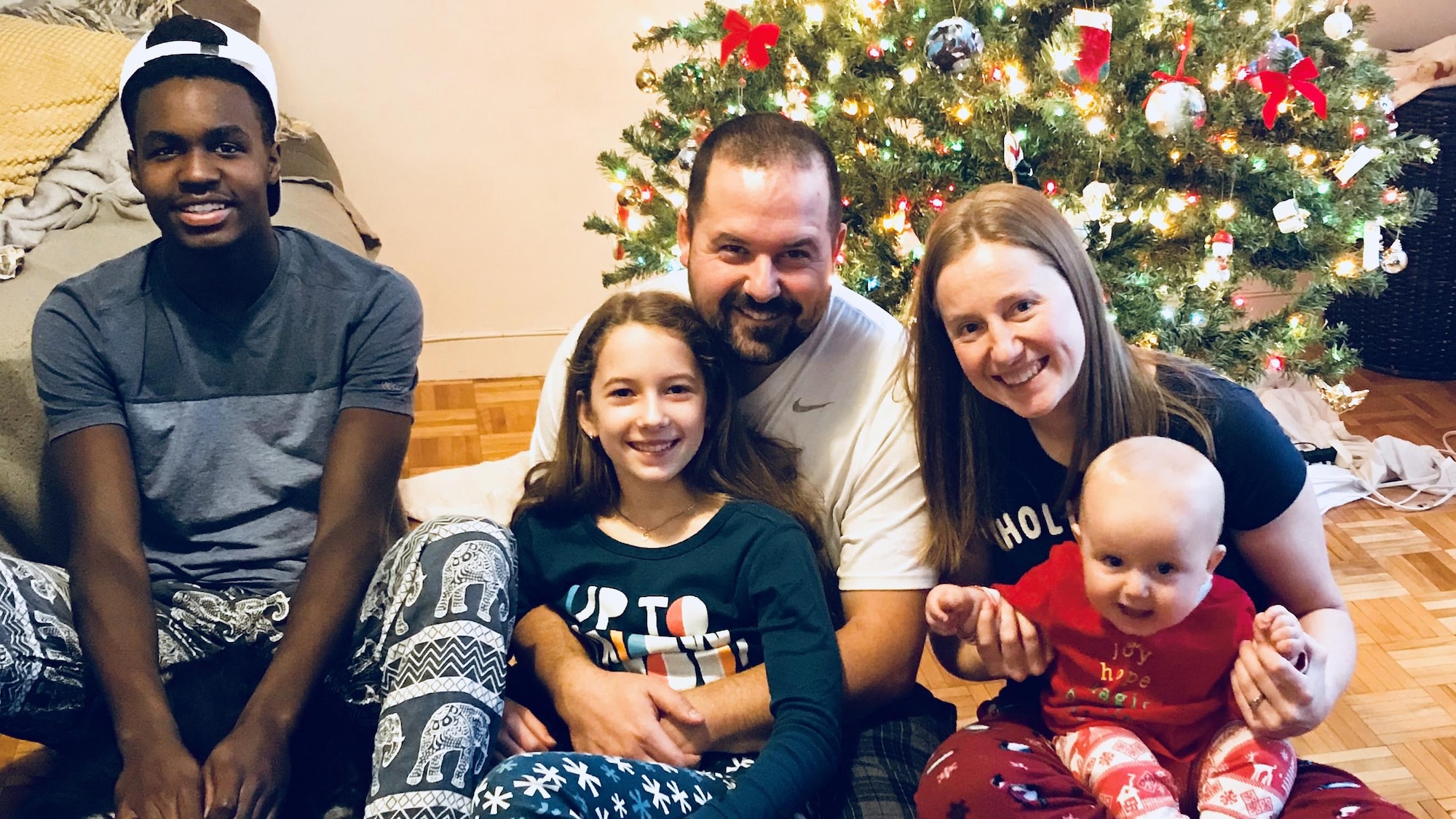 Prinzy Dessources et sa nouvelle famille sont assis sur le plancher devant leur arbre de Noël.