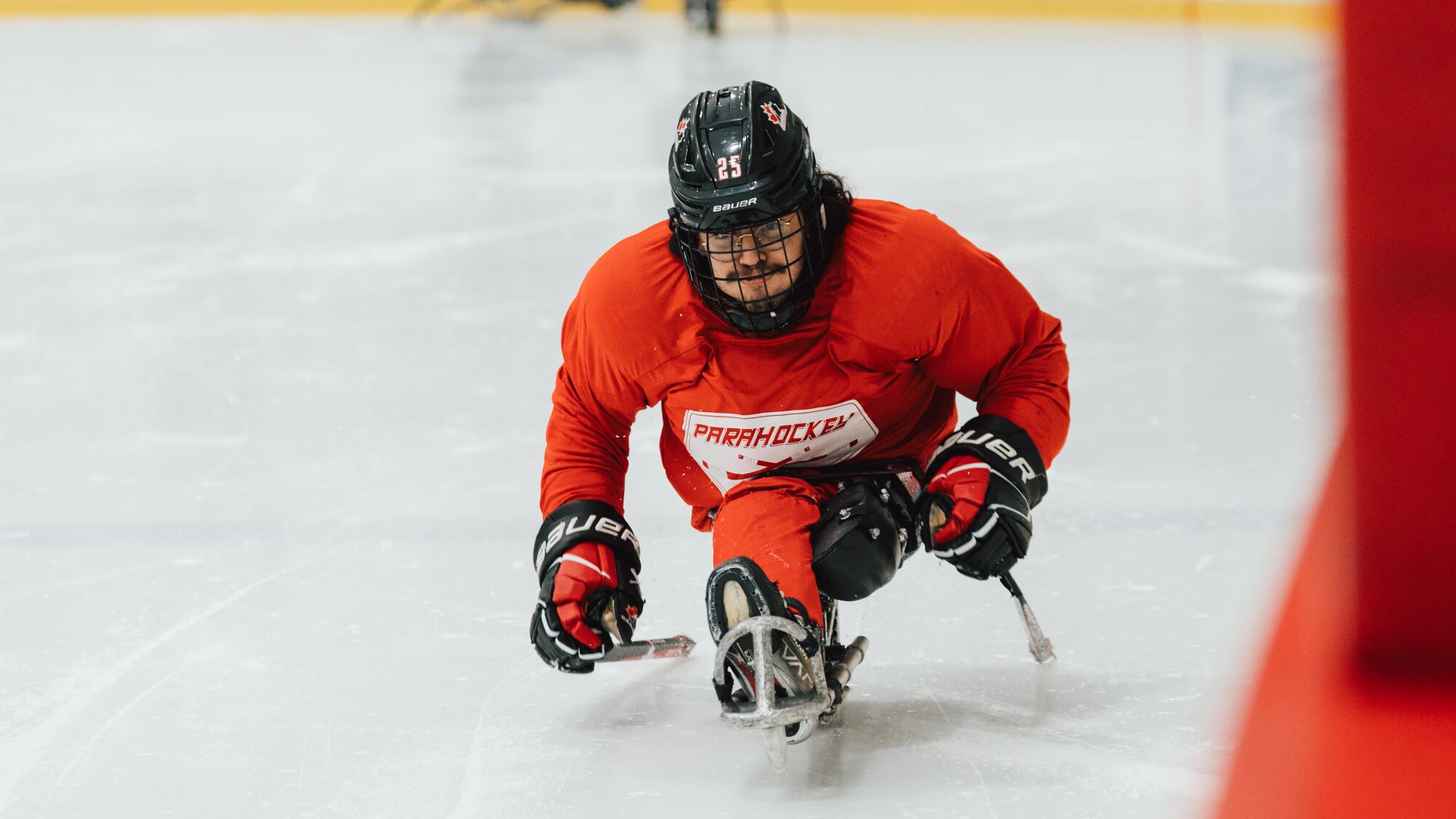 Un joueur de parahockey en rouge se propulse vers l'avant sur sa luge