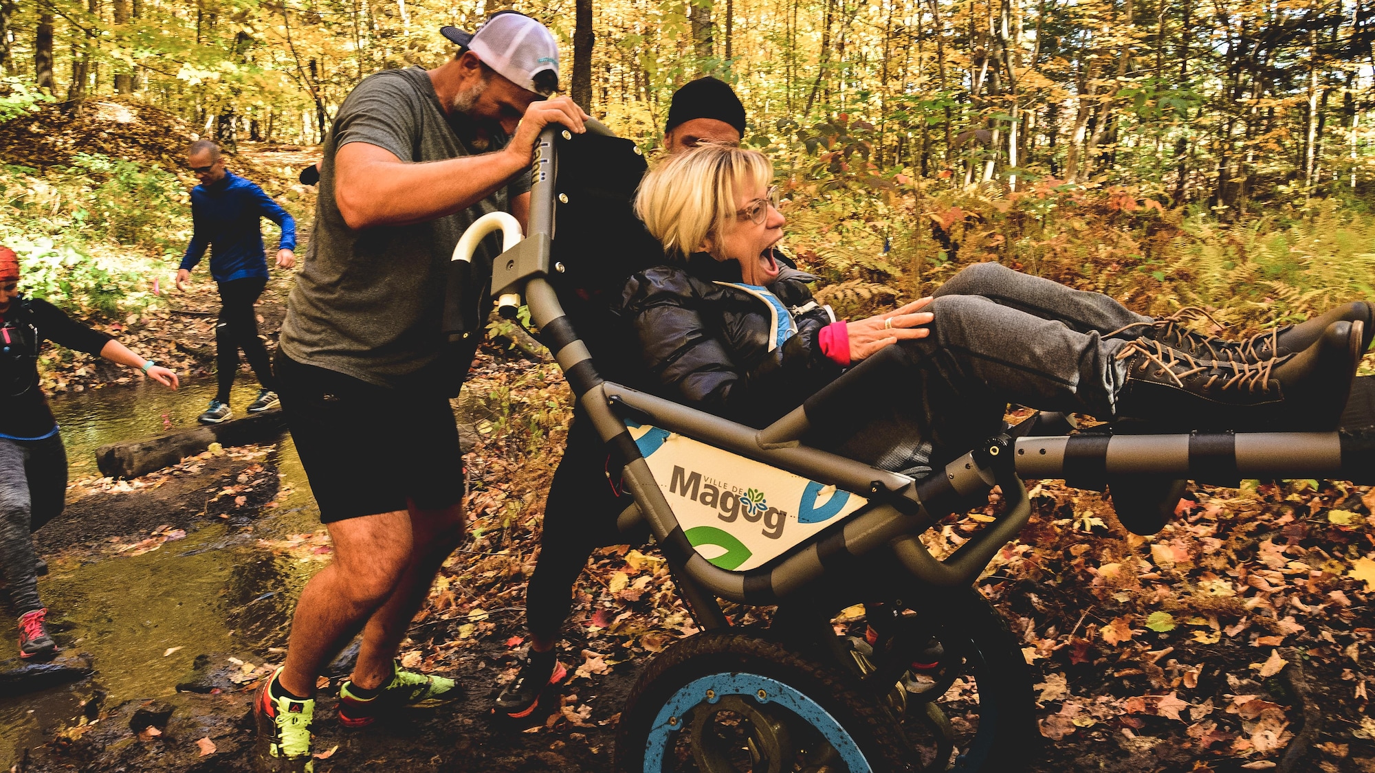 Steve Charbonneau et un autre homme poussent le chariot adapté d'une personne handicapée pendant une randonnées en forêt.