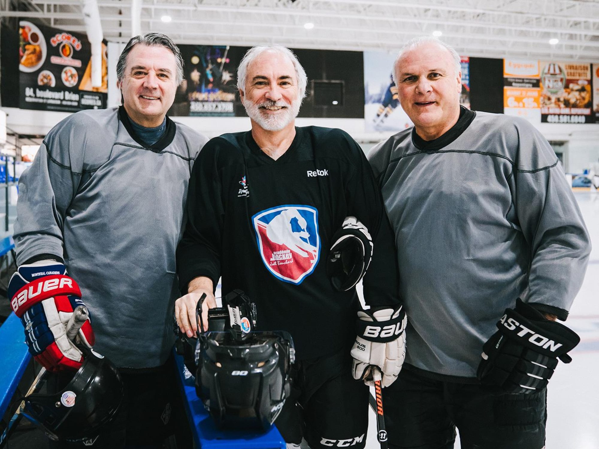 Trois hommes qui portent un uniforme de hockey regardent l'appareil photo en souriant.