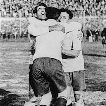 Trois joueurs de soccer s'enlacent et célèbrent sur un terrain dans un stade.