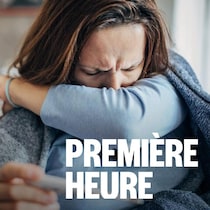 Une femme tousse dans son coude. Elle tient dans l'autre main un thermomètre.