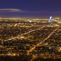 Une vue aérienne de l'Est de Montréal la nuit avec de nombreuses lumières, dont le toit du stade olympique.