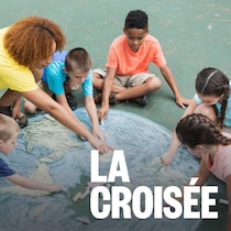 Une monitrice de camp d'été est avec cinq enfants d'âge scolaire. Ils dessinent une grande image de la terre en craie.
