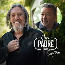 Serge Fiori en train de sourire à grandes dents en regardant droit dans l'objectif, aux côtés d'un médaillon affichant le visage de Normand Brathwaite.