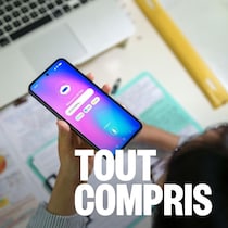 Un adolescent interagit avec une IA sur son smartphone tout en étudiant à son bureau, entouré d'un ordinateur portable, de notes et de fournitures scolaires.