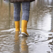 Une personne marche avec des bottes de pluie sur une rue inondée.