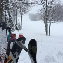 Des skis sont installés à la verticale devant une piste de ski enneigée.