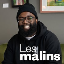 Un homme souriant qui pose assit sur un fauteuil.