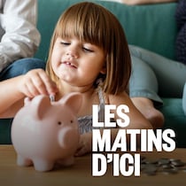 Une jeune fille qui met des pièces de monnaie dans une tirelire. Des adultes sont assis derrière elle sur un fauteuil.
