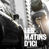 Une personne à vélo qui circule sur une route où se trouvent aussi des autos.