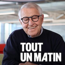 Michel Bergeron est assis à une table et il sourit.