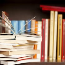 Une pile de livres sur une étagère avec un livre ouvert et des livres rangés en arrière-plan.
