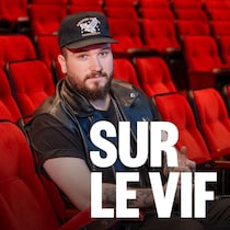 Justin Legacy, souriant, assis sur un siège d'une salle de spectacle.