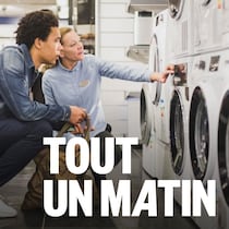 Un consommateur observe différents modèles de laveuse avec une vendeuse dans un magasin d'électroménagers.