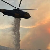 Un hélicoptère largue de l'eau sur des montagnes en flammes.   