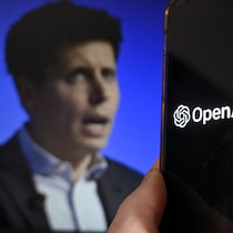 Sam Altman derrière un écran de téléphone montrant le logo d'OpenAI.