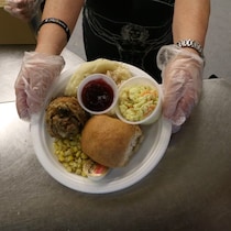 Une personne bénévole montre une assiette composée de dindes, de salade, de sauce à la canneberge et d'un petit pain.