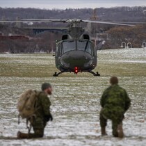 Deux membres militaire accroupis avec au loin l'hélicoptère  CH-146 Griffon de l'Aviation royale canadienne.