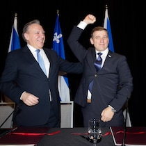Deux hommes en complet pendant une conférence de presse. Andrew Furey lève le bras droit, son poing fermé, pendant que François Legault lui tapote le dos.