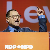 Avi Lewis prononce un discours derrière un lutrin du N P D.