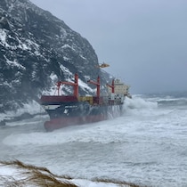 Un navire près de rochers, de grosses vagues, un hélicoptère au-dessus du bateau, dans une température hivernale inhospitalière.
